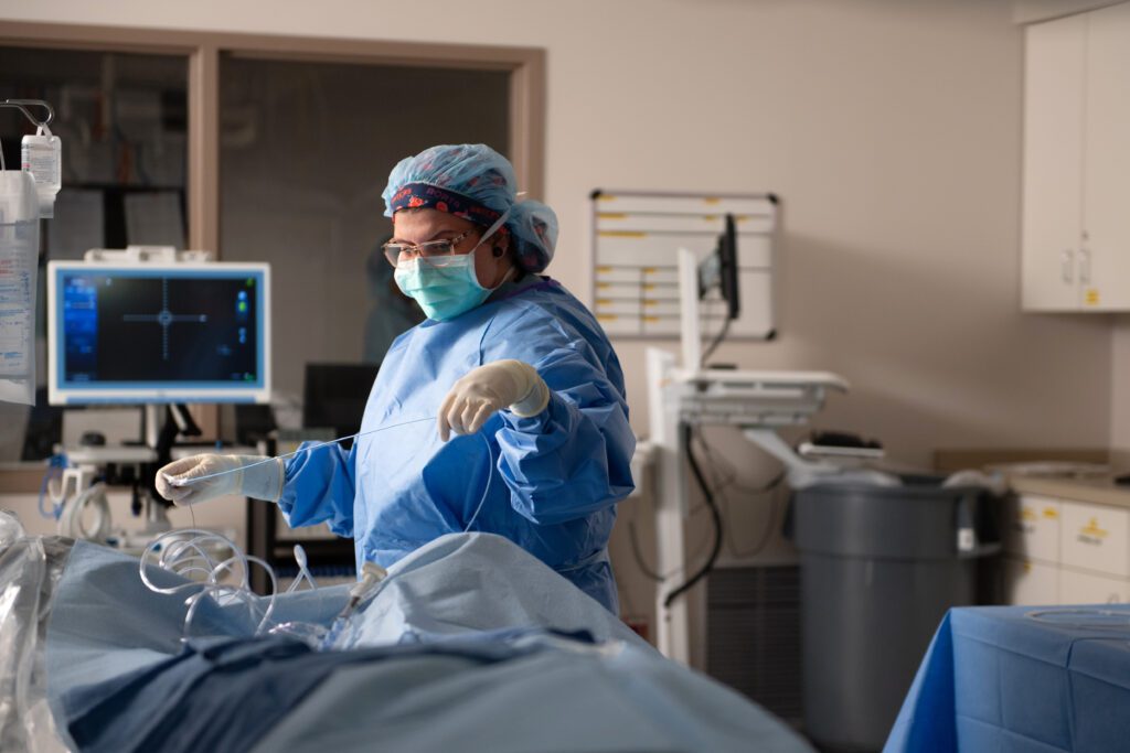 Cath Lab technologist in full protective equipment preparing specialized catheter equipment for a minimally invasive heart procedure.